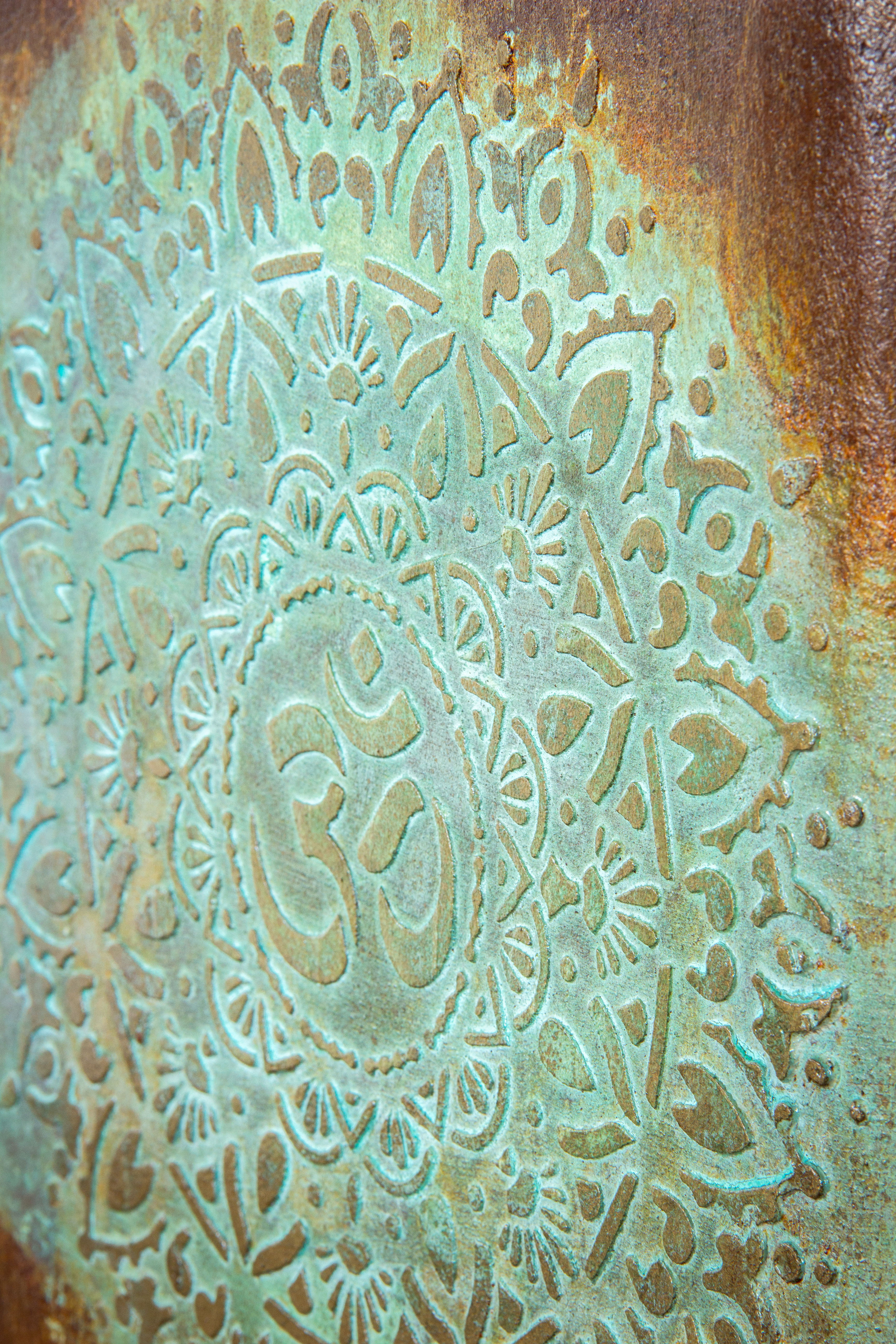 Ręcznie wykonana osłonka z symbolem OM w reliefie, efekt kortenu z turkusową patyną